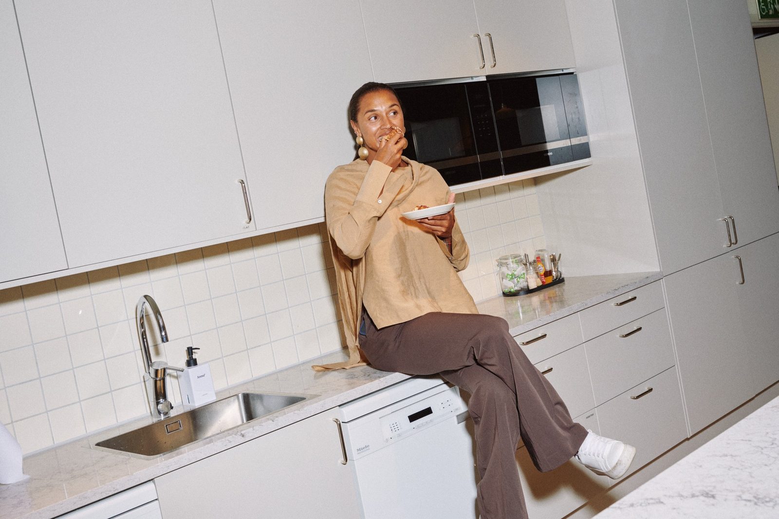 Kvinna sitter på köksbänken i ett personalkök och äter